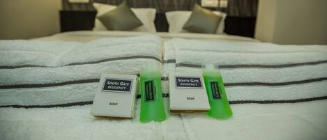 Una cama bien hecha con dos botellas verdes de jabón del South Gate Residency y una almohada.