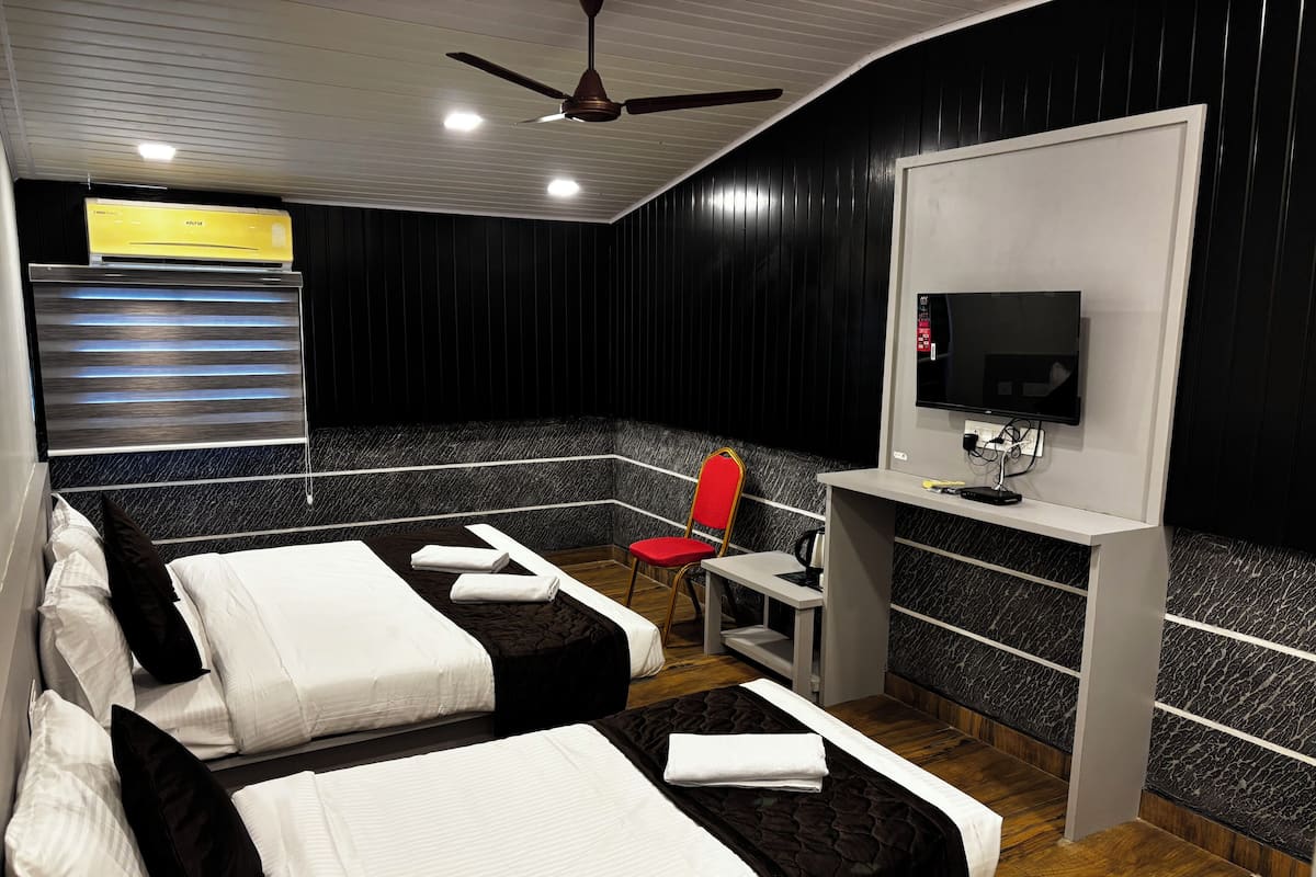 A hotel room with two beds, a desk, a chair, a television, and a ceiling fan.