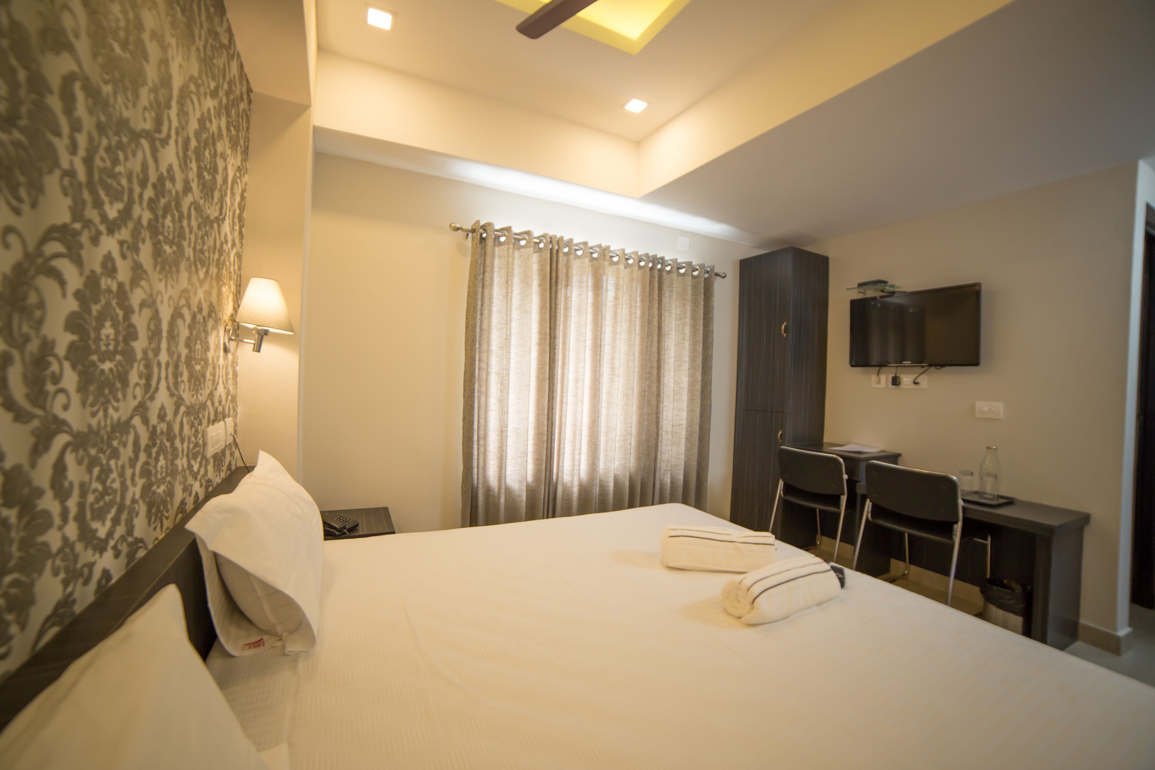 A hotel room with a bed, a desk, a chair, a TV, and a window with curtains.
