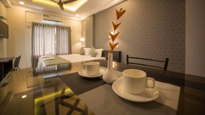 Ein Hotelzimmer mit Bett, Esstisch, Tassen und einer Vase, sowie einem Deckenventilator.