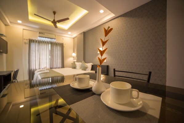 A hotel room with a bed, a dining table with cups and a vase, and a ceiling fan. - South Gate Residency (Kanayannur)
