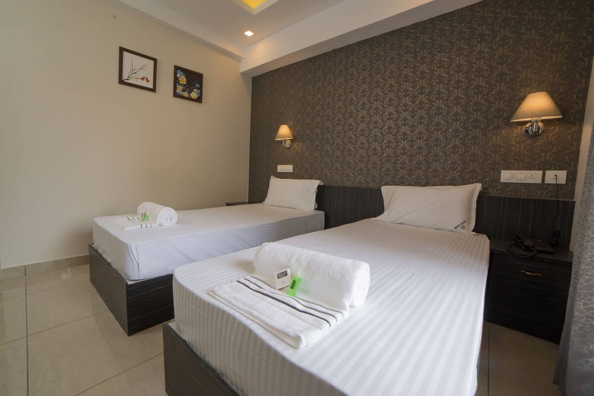 A hotel room with two beds, a nightstand, a lamp, and a wall with framed pictures.