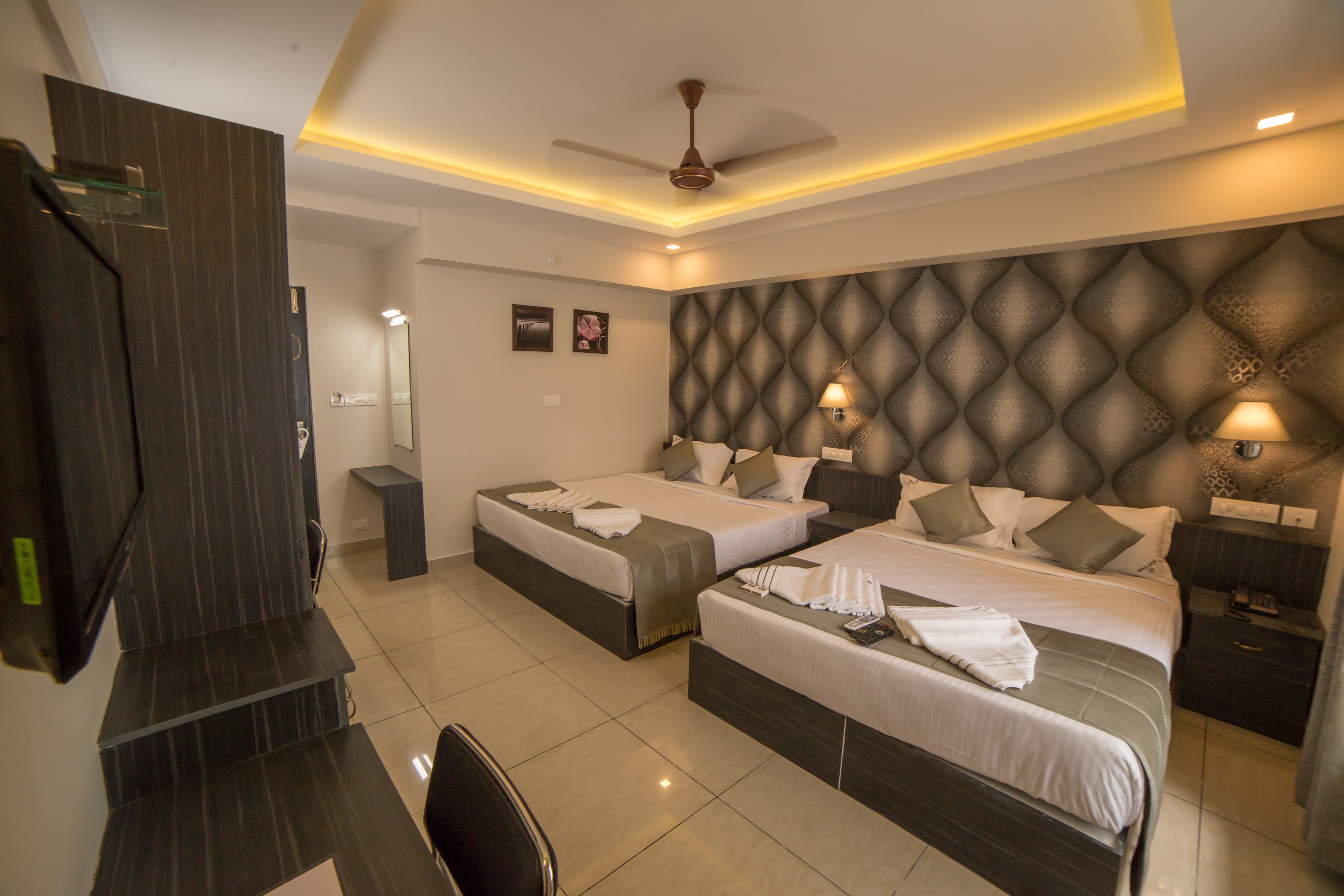 A hotel room with two beds, a desk, a TV, and a ceiling fan.