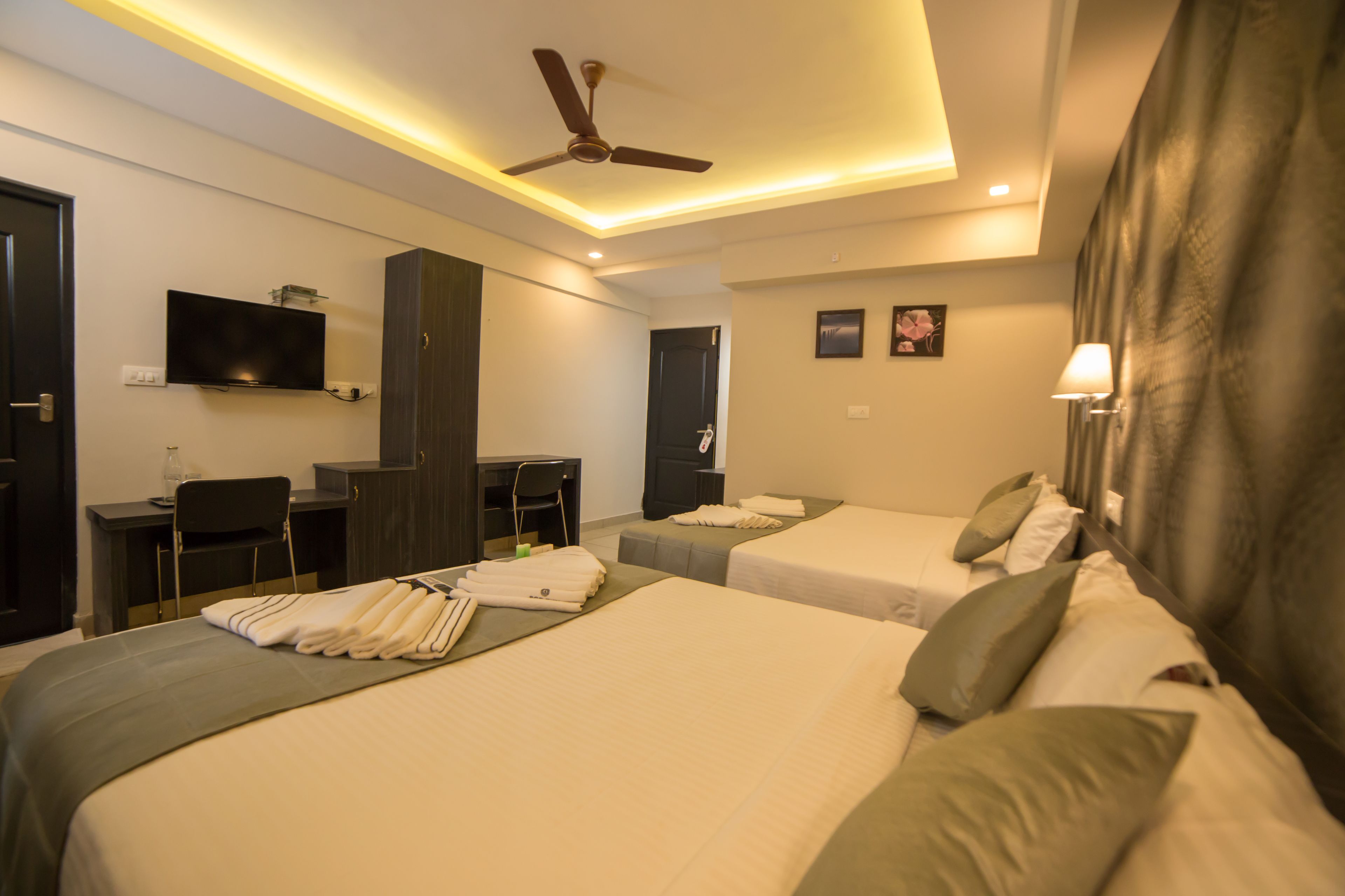 A hotel room with two beds, a desk, a TV, and a ceiling fan.