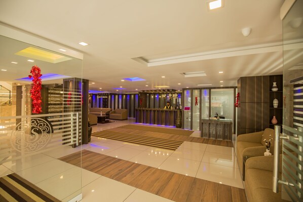 A modern lobby with a reception desk, seating area, and a decorative wall. - South Gate Residency (Kanayannur)