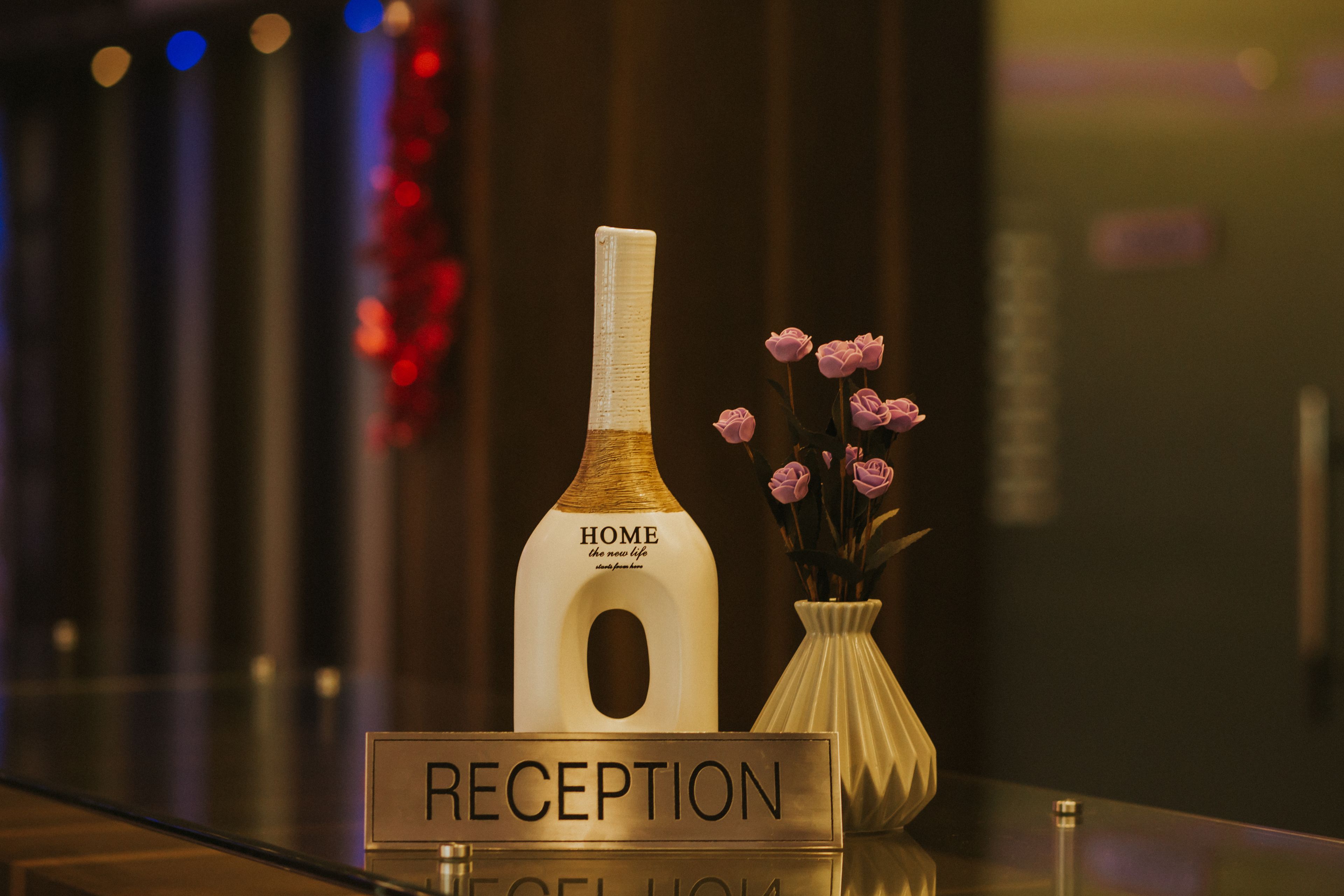 A reception area with a sign labeled "RECEPTION" and a bottle labeled "HOME the new life" with pink flowers in a vase.