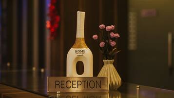 A reception area with a sign labeled "RECEPTION" and a bottle labeled "HOME the new life" with pink flowers in a vase.