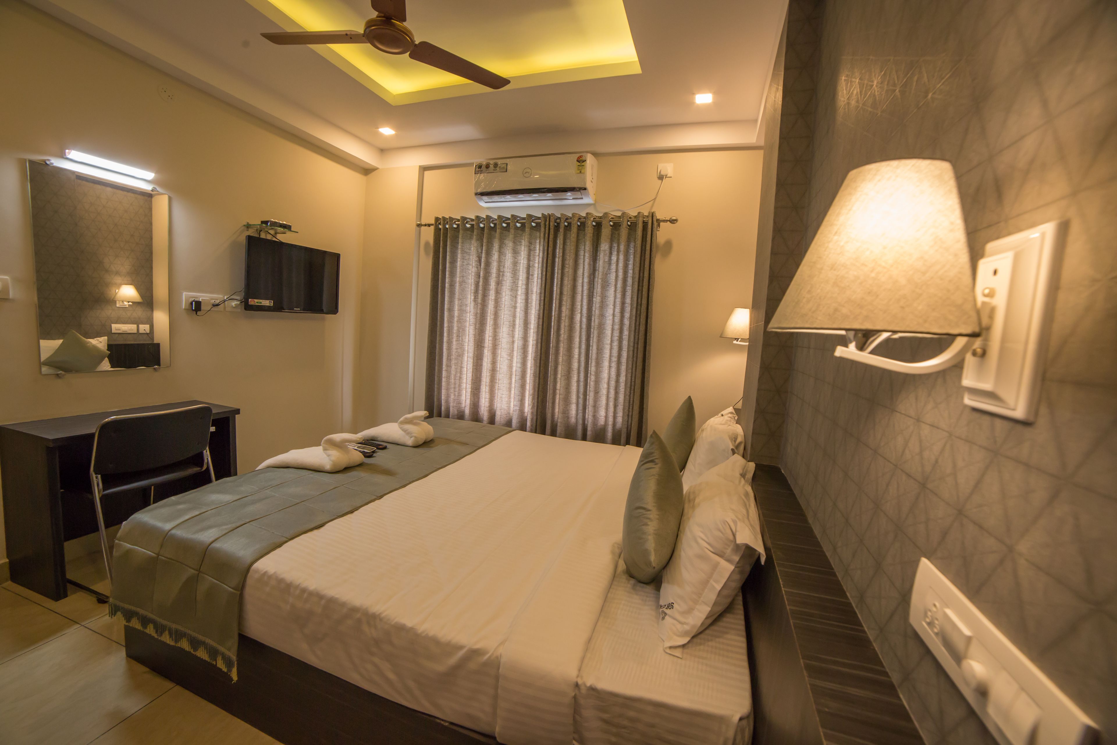 A hotel room with a bed, desk, and ceiling fan.