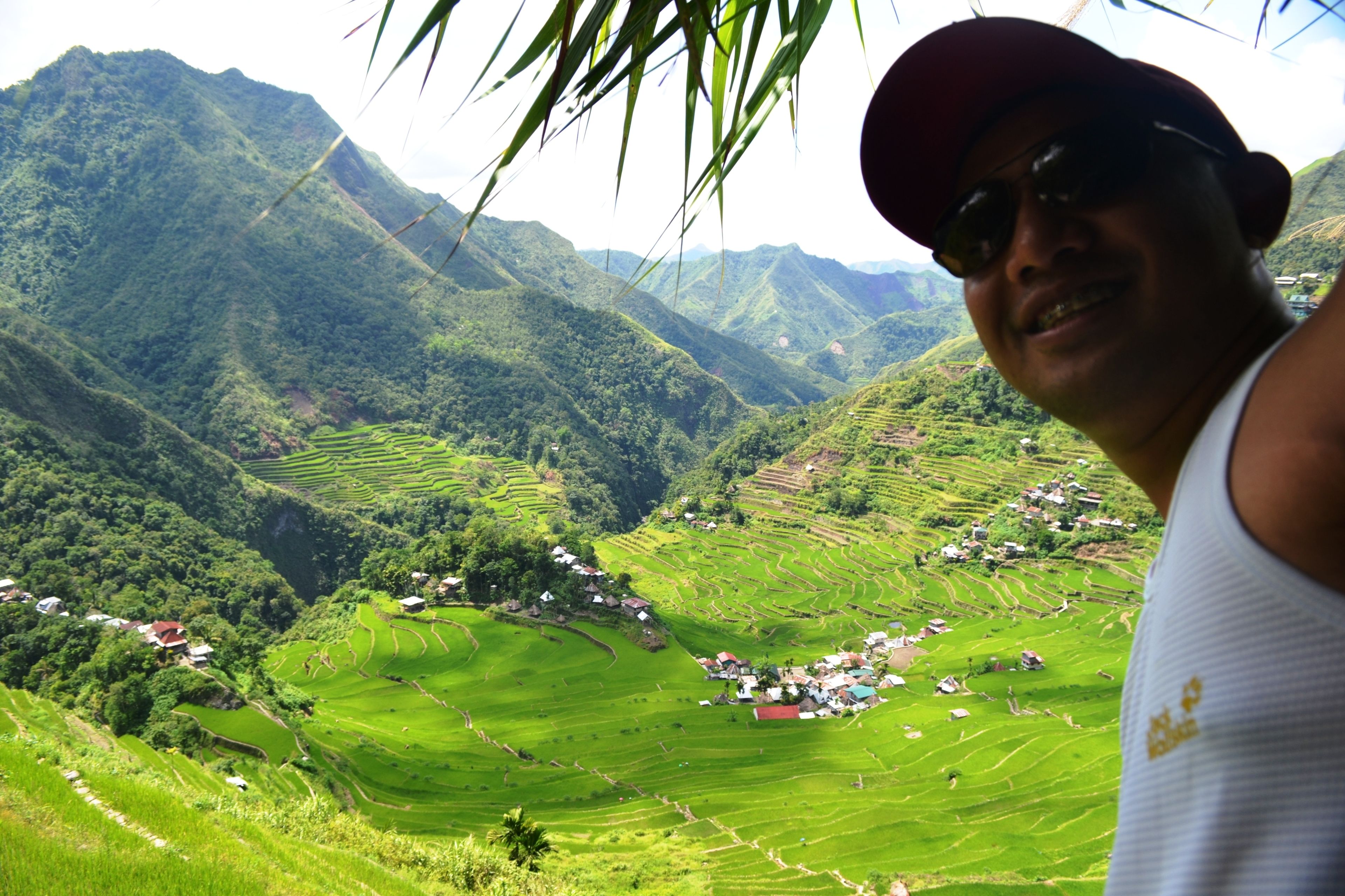 A person standing in front of terraced rice fields with a mountainous backdrop.