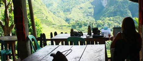 A table with a teapot, chairs, and a view of terraced fields and mountains.