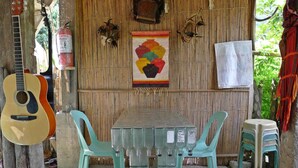 A rustic outdoor dining area with a bamboo wall, a guitar, and a colorful painting.