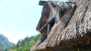 A traditional thatched-roof house with a visible window and a wooden door. - Ramons Native Homestay and Restaurant (Banaue)
