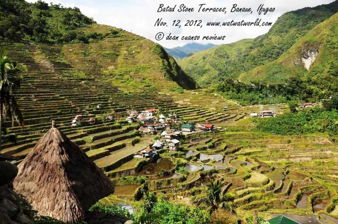 Terraced rice fields with a village and a thatched-roof structure.