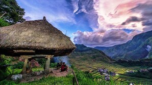 A traditional thatched-roof hut with a view of terraced fields and mountains in the background.