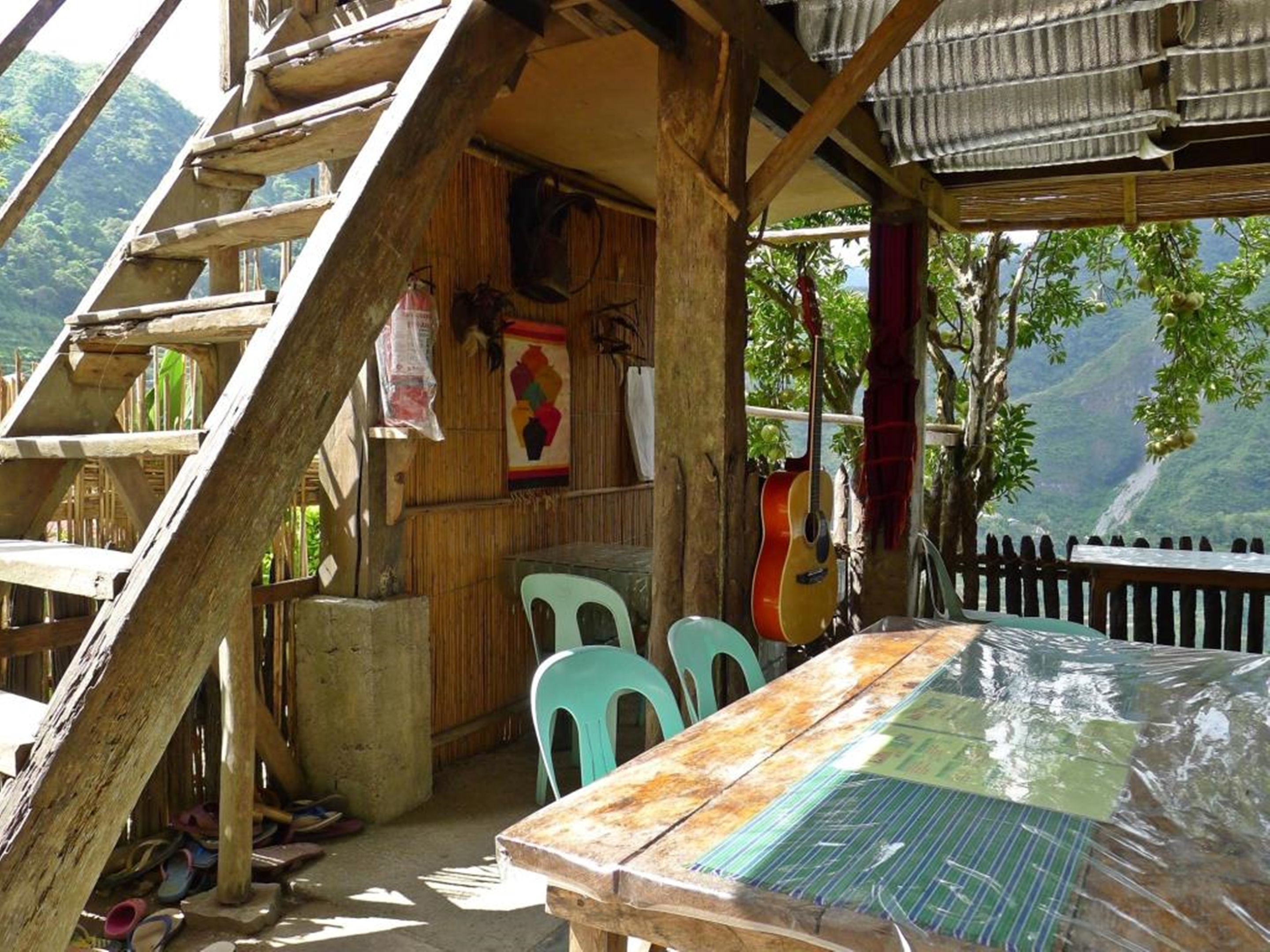 A rustic wooden structure with a table and chairs, a guitar, and a view of a mountainous landscape.