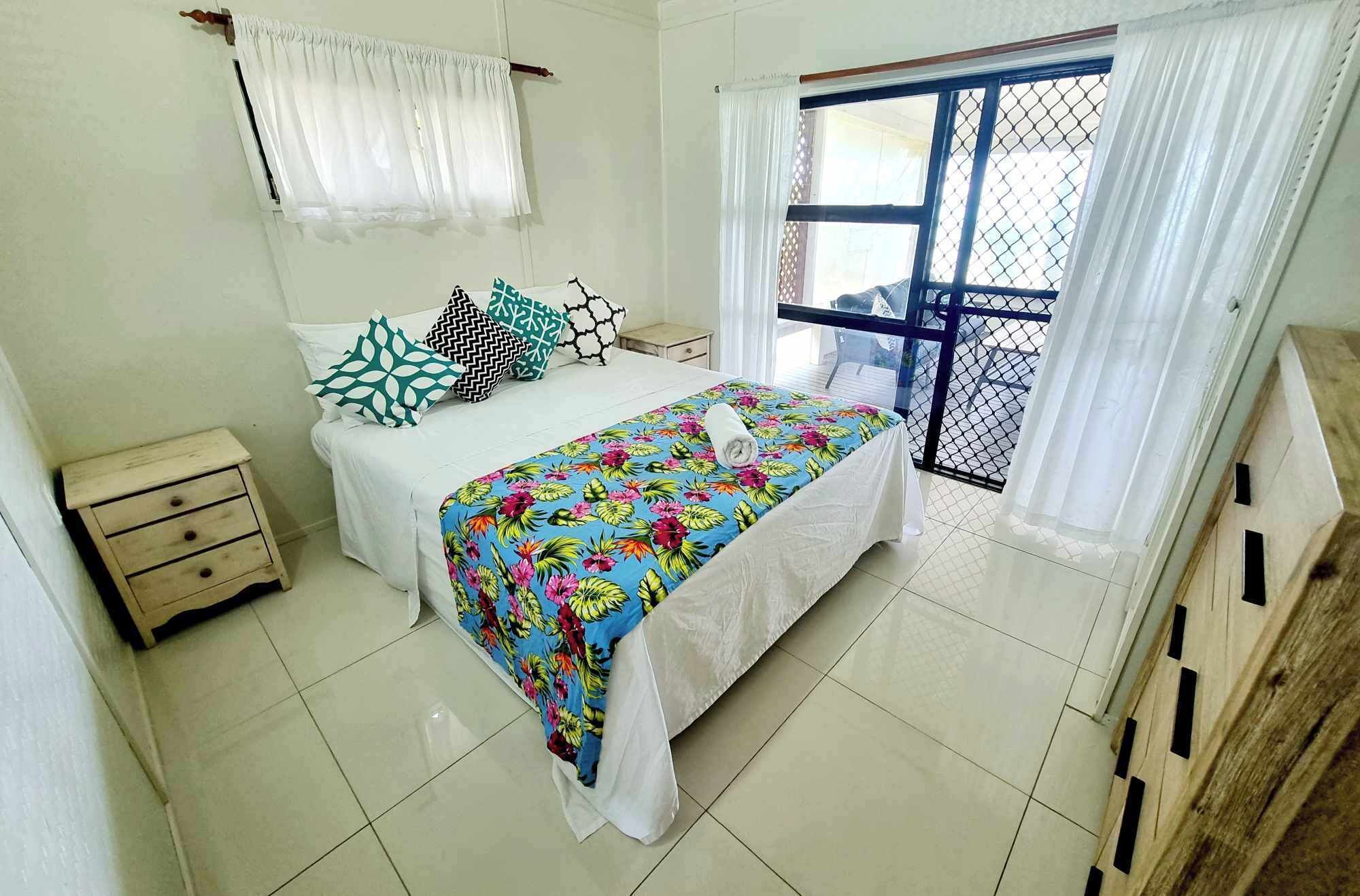A bedroom with a bed, a nightstand, a window with curtains, and a view of the outside.