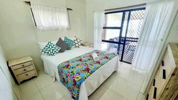A bedroom with a bed, a nightstand, a window with curtains, and a view of the outside.