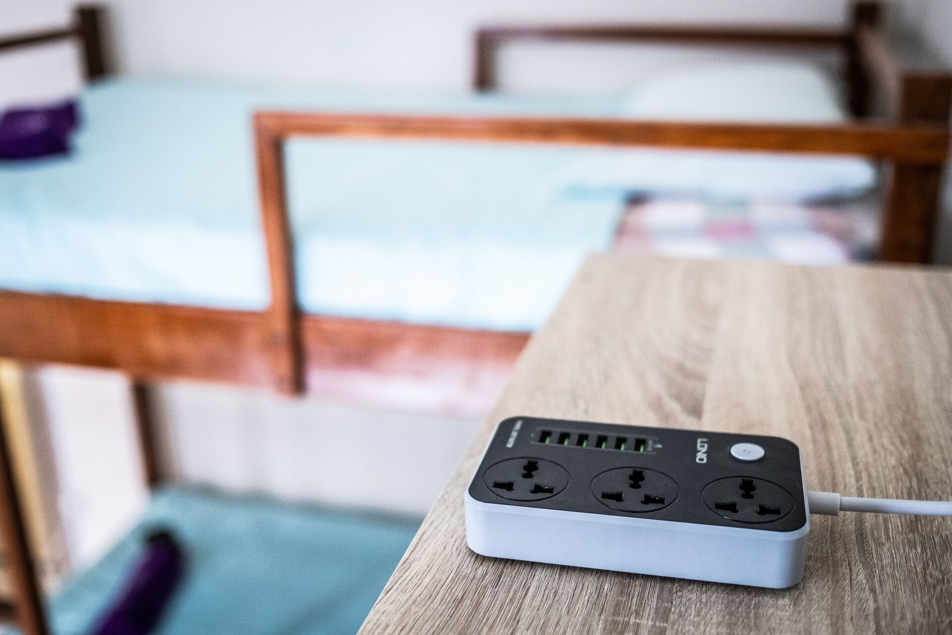 A power strip on a wooden table with a bed in the background.