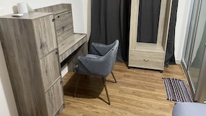 Una habitación con un armario de madera, una silla gris, una mesita y un mueble espejo.