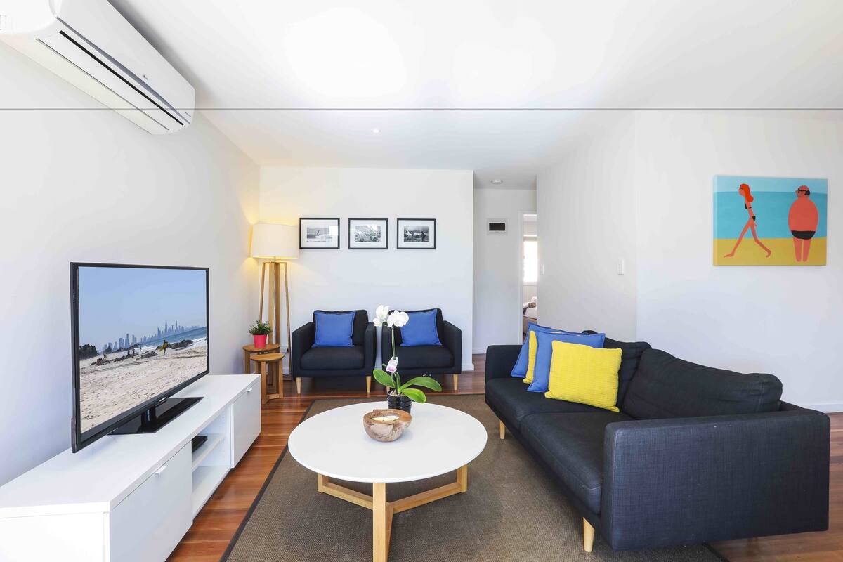 A modern living room with a flat-screen TV, two sofas, a coffee table, and framed pictures on the wall.