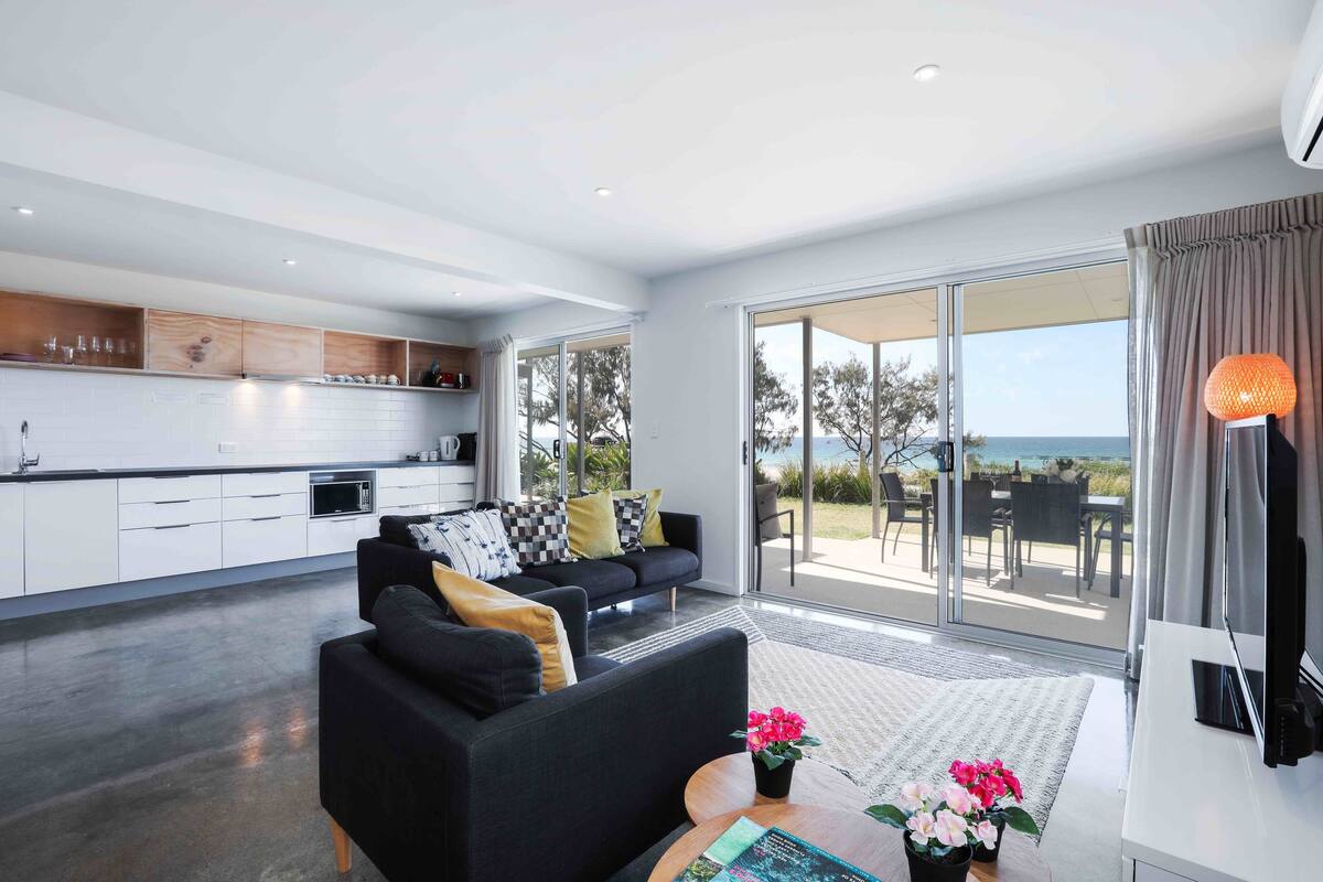 A modern kitchen with white cabinets, a black sofa with cushions, and a dining area with a table and chairs.
