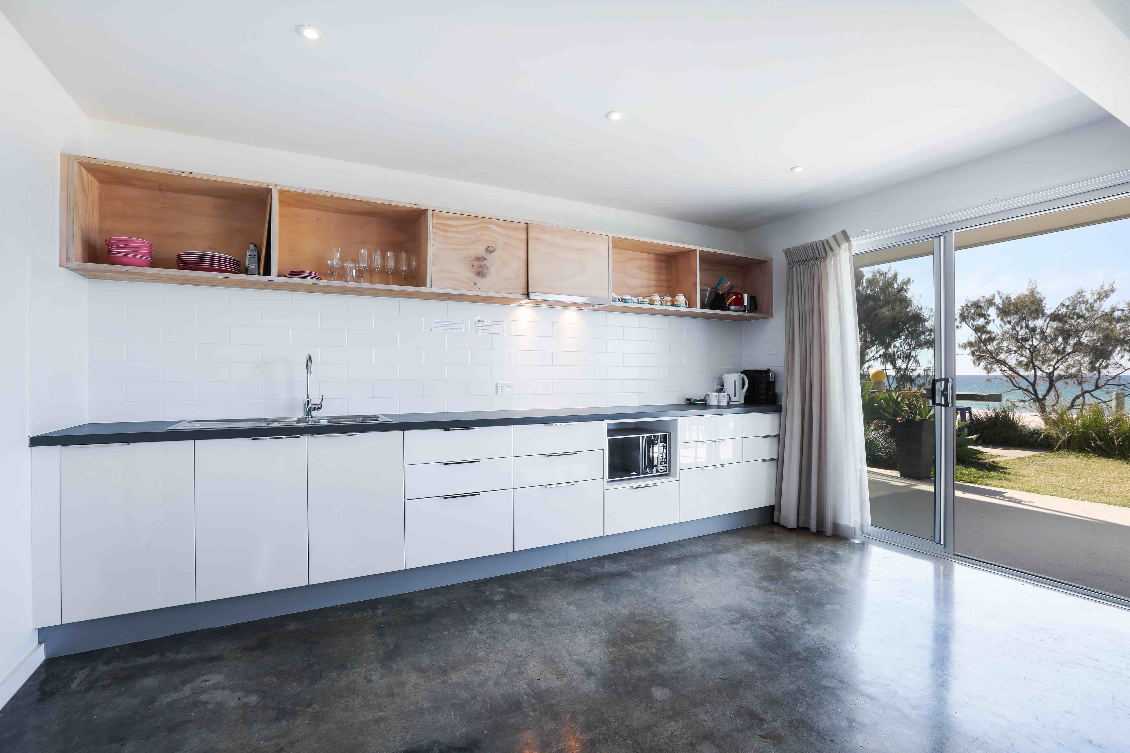 A modern kitchen with white cabinets, a black countertop, and wooden shelves.