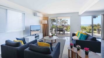 Ein modernes Wohnzimmer mit Flachbildfernseher, zwei Sofas, einem Couchtisch und einem Balkon mit Meerblick.