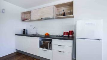 A modern kitchen with white cabinets, a built-in microwave, a stainless steel sink, and a red kettle.