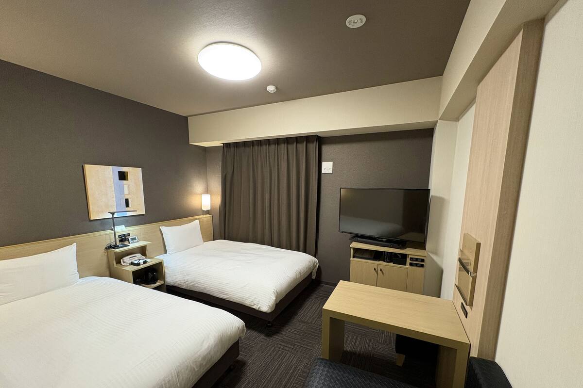 A hotel room with two beds, a desk, a TV, and a mirror.