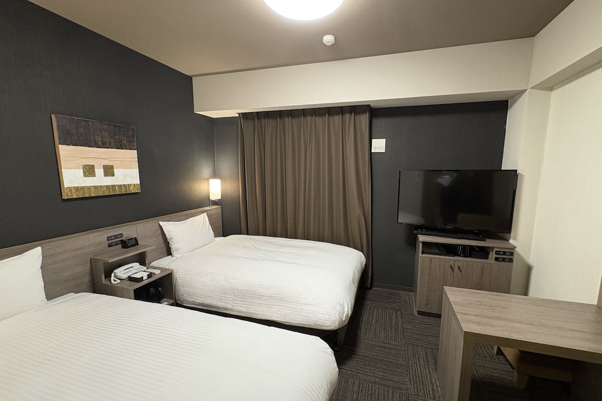 A hotel room with two beds, a desk, a TV, and a painting on the wall.