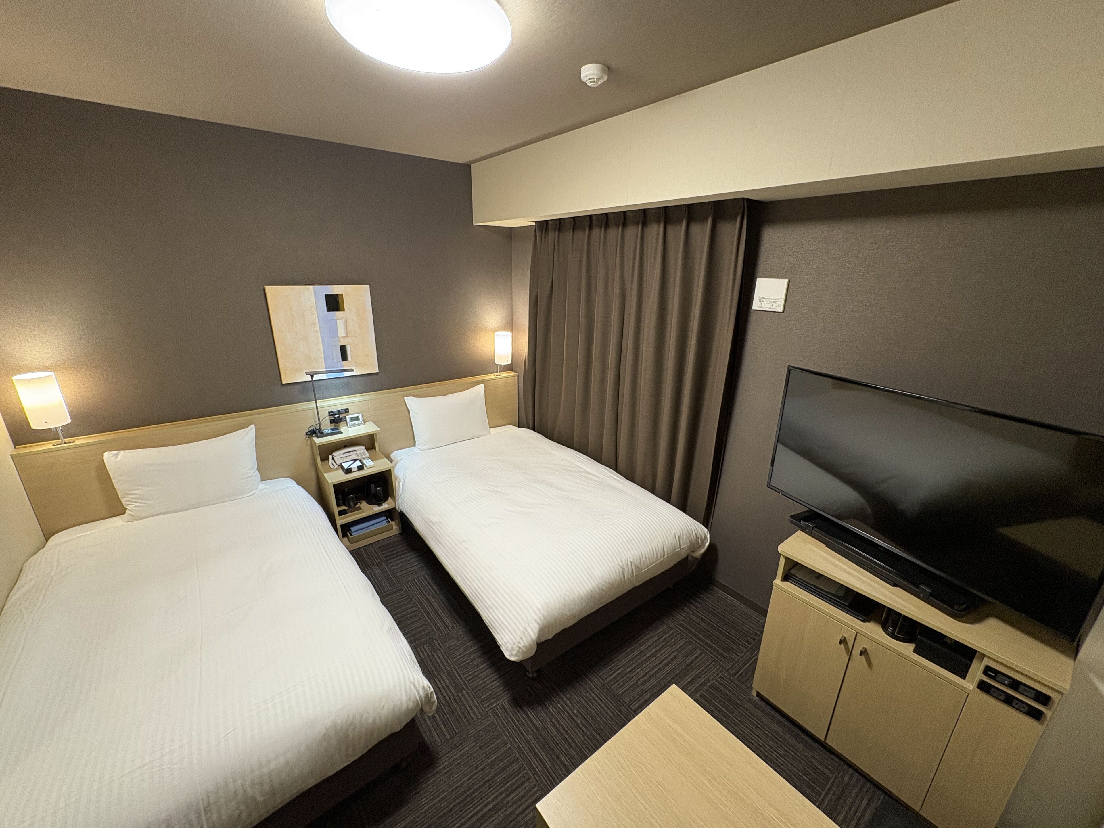 Een hotelkamer met twee bedden, een bureau met een lamp, een televisie en een minibar.