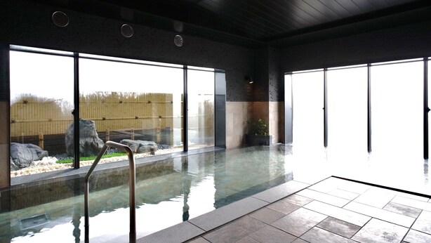 En inomhuspool med väggar av genomskinligt glas, ett stengolv och ett bambustaket som syns genom fönstren.