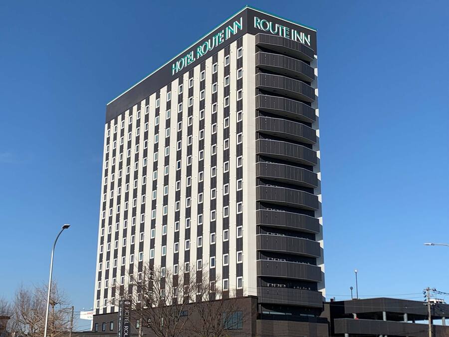 A tall, modern hotel building with the name "Hotel Route Inn" on the top. It has multiple floors with a consistent window pattern and a flat roof.