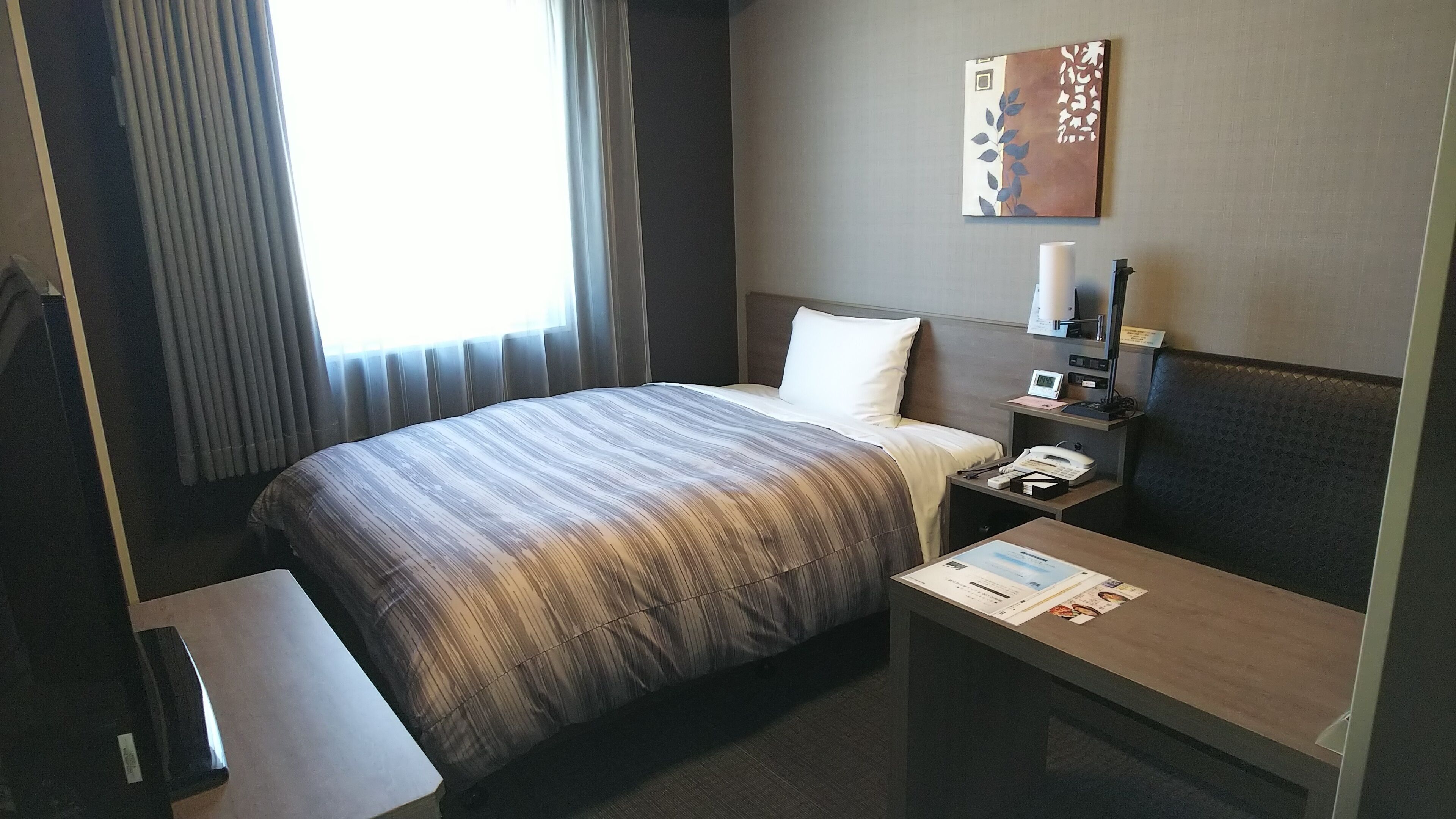 A hotel room with a bed, bedside table, lamp, and a wall-mounted artwork.