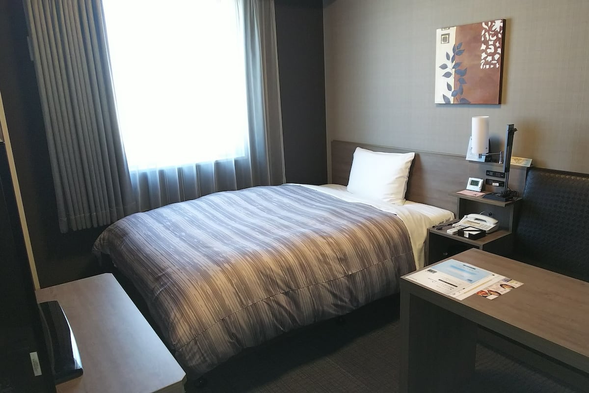 A hotel room with a bed, bedside table, lamp, and a wall-mounted artwork.