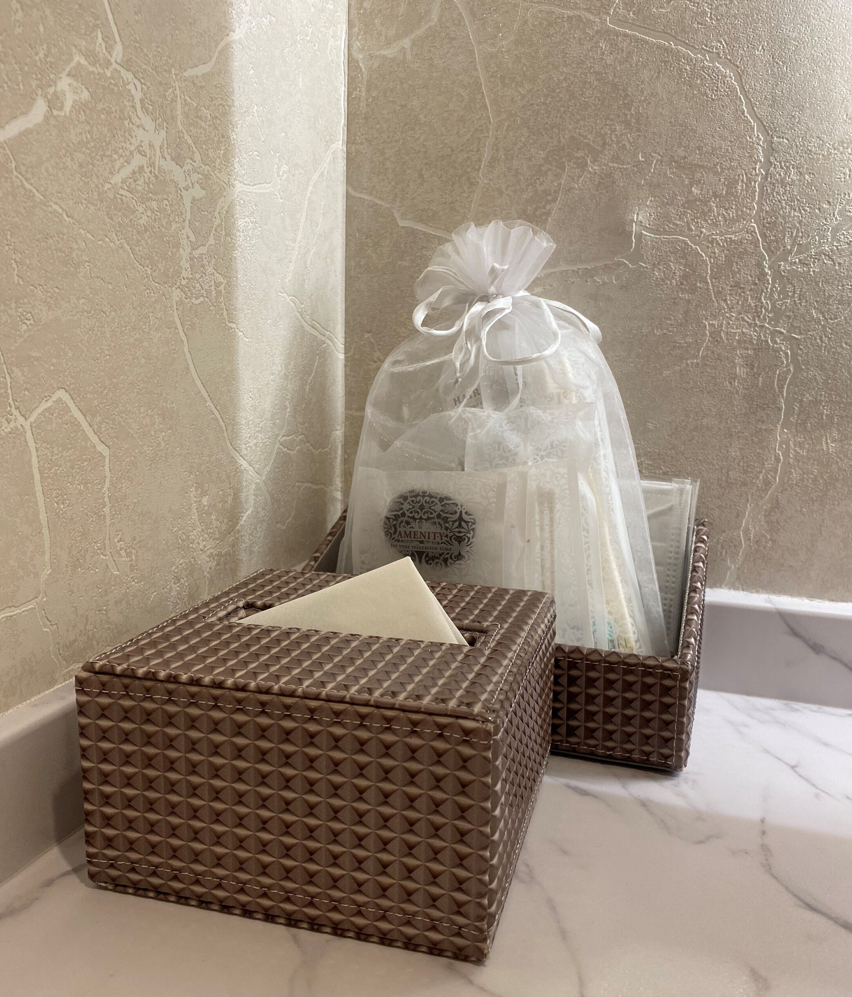 Ein Badezimmer mit Marmorplatte, einer braunen strukturierten Schachtel und einer transparenten Tasche mit Schleife.
