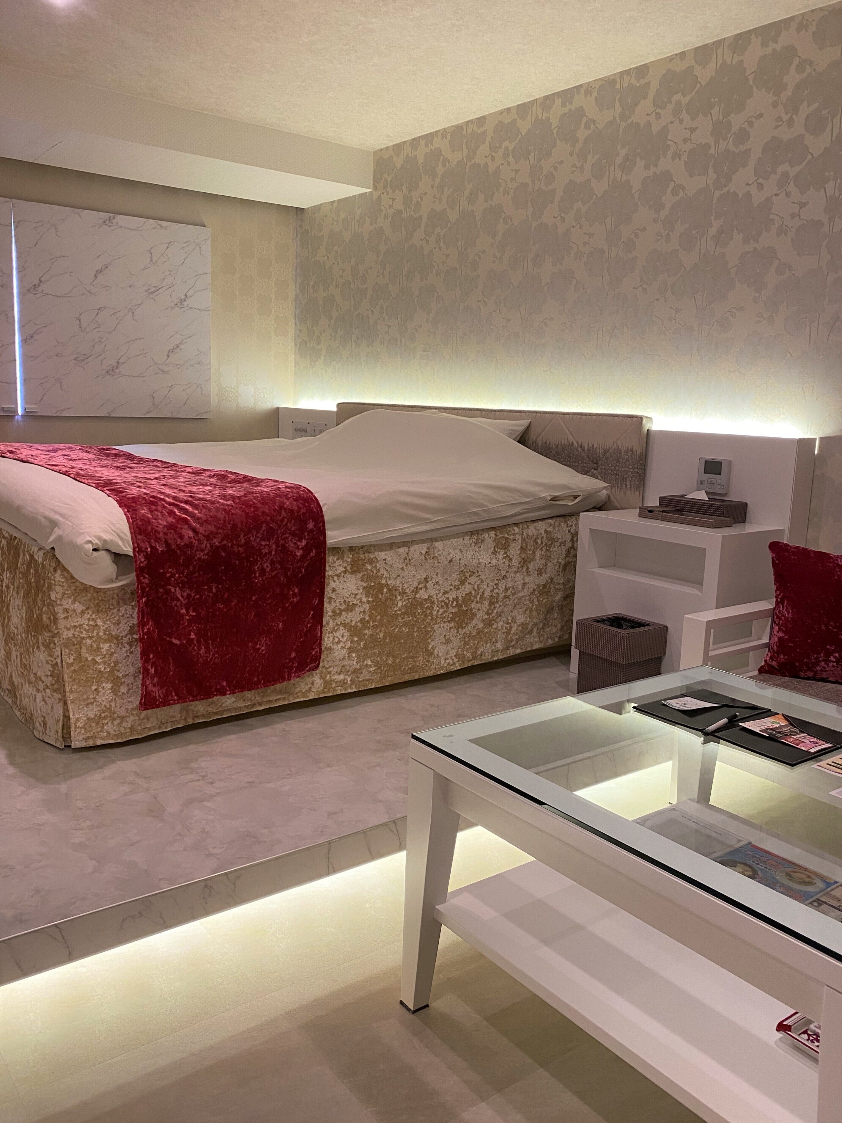 Un dormitorio moderno con una cama, una mesita de noche y una mesa de vidrio con revistas.