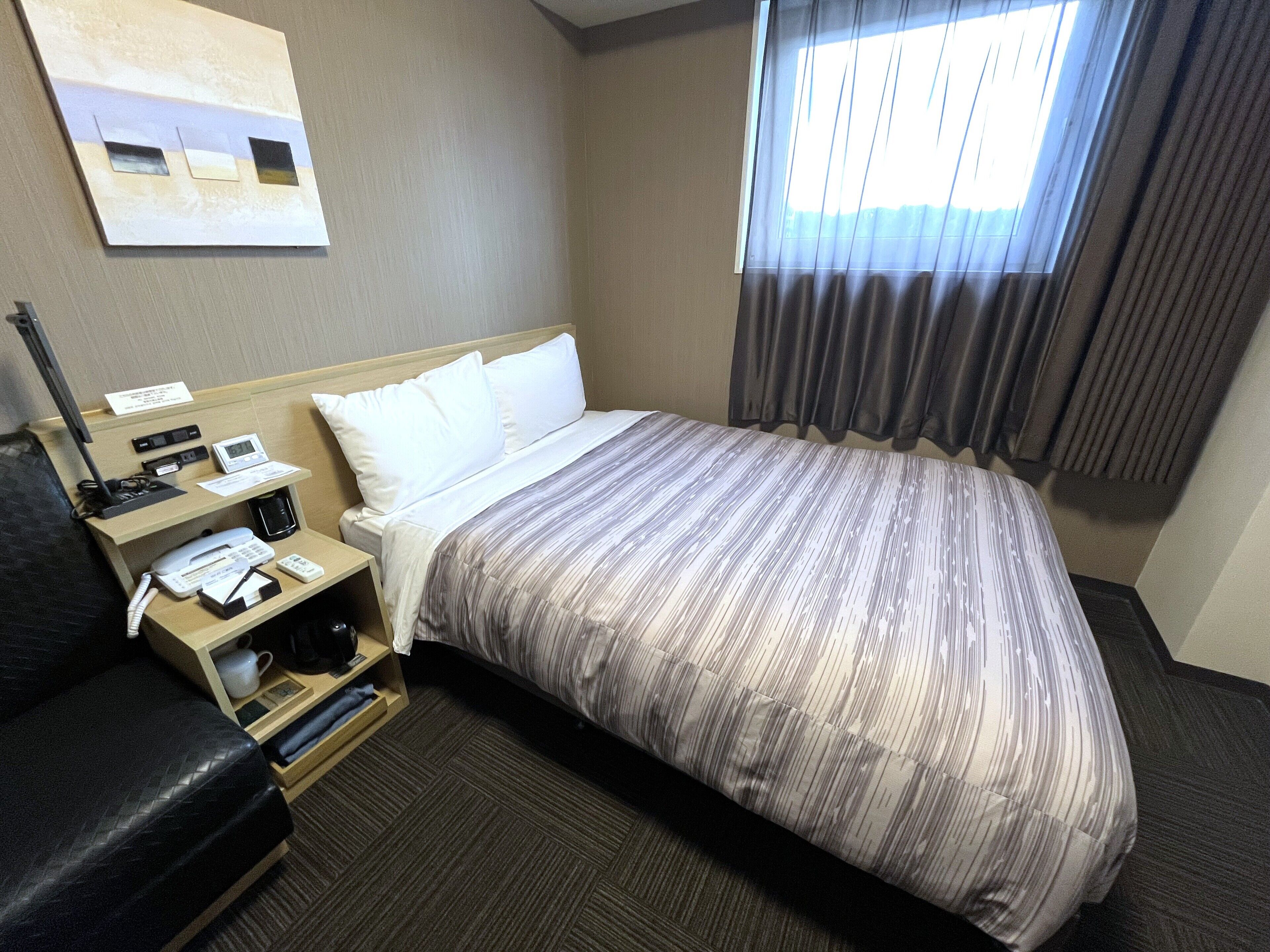 A hotel room with a bed, a desk with a phone, a lamp, and a painting on the wall.