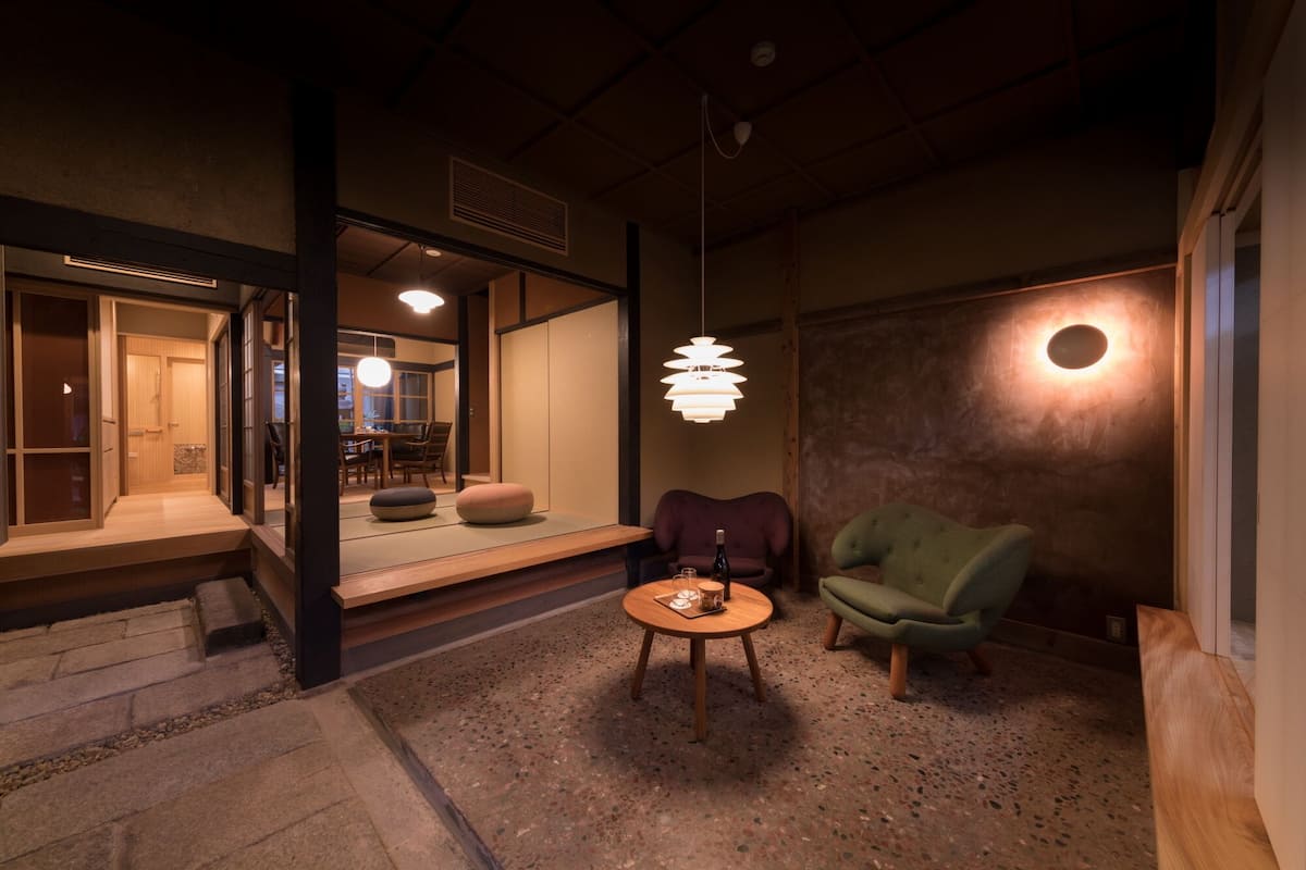 A cozy interior with a wooden floor, a round table with a bottle and glasses, and a green armchair.