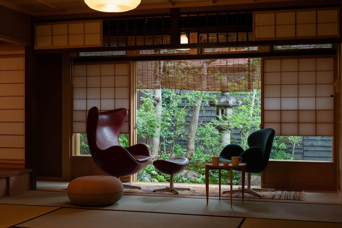 A traditional Japanese room with tatami flooring, shoji screens, and a view of greenery outside.