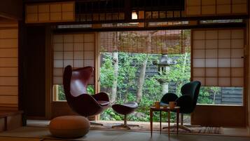 A traditional Japanese room with tatami flooring, shoji screens, and a view of greenery outside.