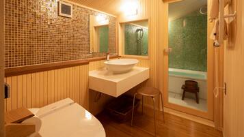 Un baño con tocador de madera, un lavamanos grande, un inodoro y una bañera visible a través de una puerta de cristal.