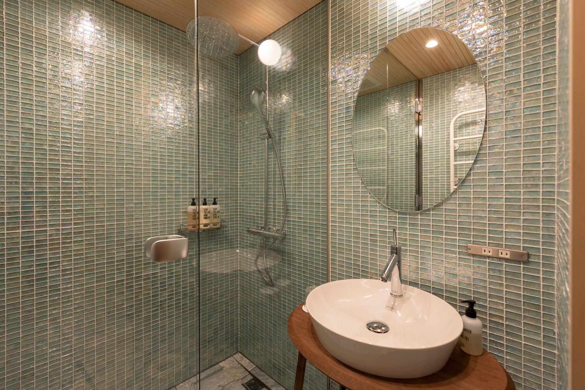 Een badkamer met een douche met glazen wand, een rond wastafel en een spiegel.