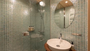 Een badkamer met een douche met glazen wand, een rond wastafel en een spiegel.