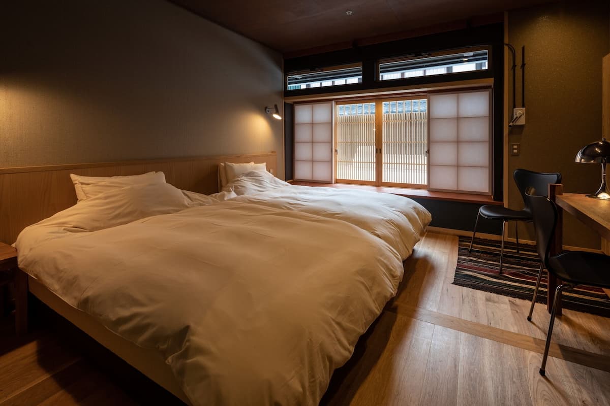 A hotel room with a large bed, a desk with a chair, and a view through a shoji screen.