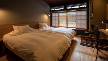A hotel room with a large bed, a desk with a chair, and a view through a shoji screen.