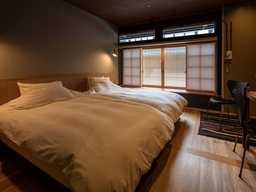 A hotel room with a large bed, a desk with a chair, and a view through a shoji screen.