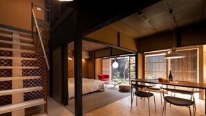 Un interior moderno con una escalera de madera, un comedor con mesa y sillas, y una cama al fondo.