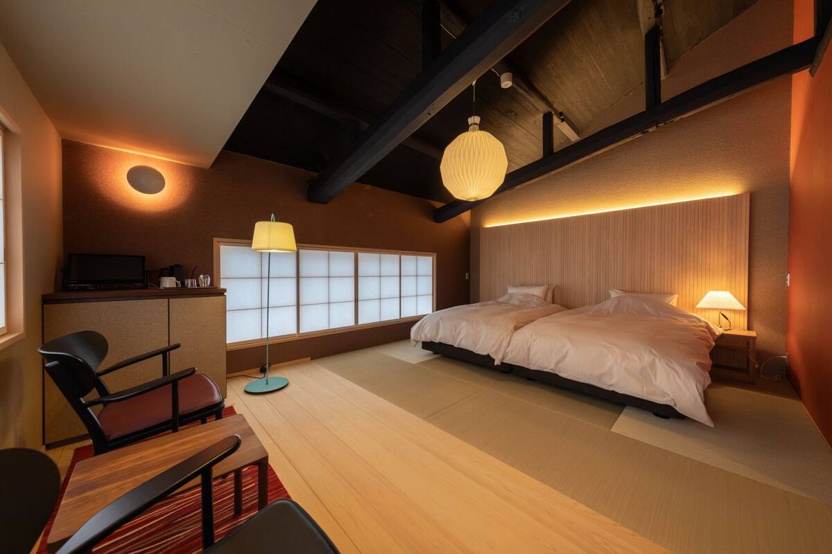 A modern hotel room with a large bed, a desk with a computer, a chair, and a traditional Japanese sliding door.