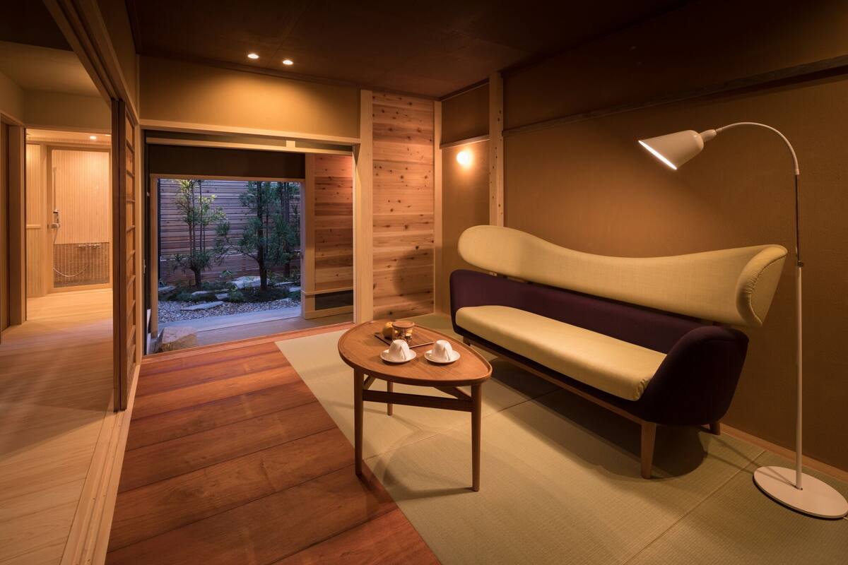 A modern interior with a wooden floor, a sofa, a table with hats, and a lamp.